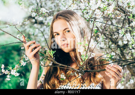 Porträt eines jungen Mädchens in der Blüte Cherry Garden, das Berühren eines Zweige, mit Blick auf die Kamera Stockfoto