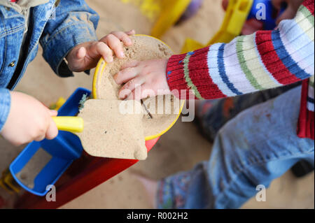 Kinder mit Schaufel und Spaten in der sandkasten draußen auf dem Spielplatz eines Kindergartens UK. Stockfoto