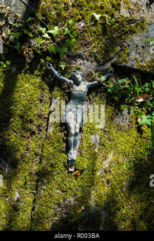 Metall Figur zeigt den gekreuzigten Jesus Christus liegen auf Bemoosten Stein Stockfoto