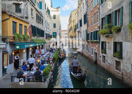 Venedig, Italien - 13 AUGUST 2017: Restaurant mit Bürgersteig Tische mit Menschen zum Abendessen und Gondel vorbei in den Kanal Stockfoto