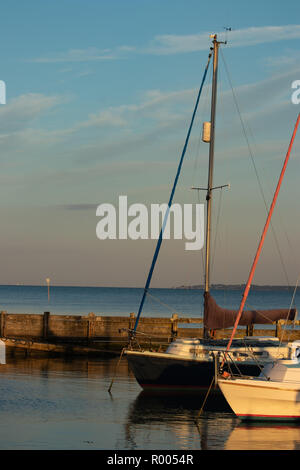 Segeln Boote im Yachthafen bei Sonnenuntergang auf dem ruhigen Wasser widerspiegeln Stockfoto