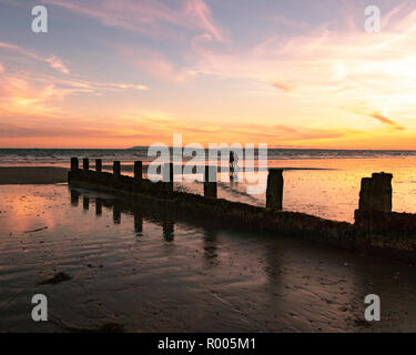 Paar bei einem Spaziergang auf dem Sand hinter einem hölzernen Strand buhnen am Strand bei Sonnenuntergang Stockfoto