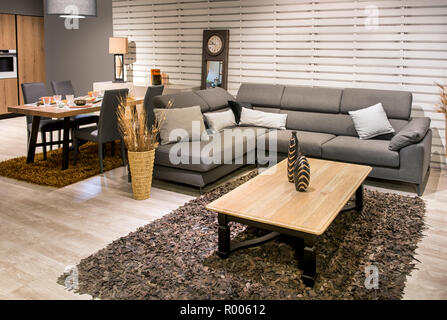 Geräumige offene Küche, Esszimmer und Wohnzimmer mit grauen gepolsterten Sofa, Teppich, Tisch und Holzboden in einem modernen Haus Stockfoto