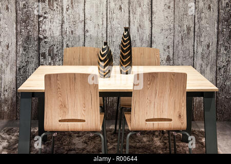 Moderne Holz- Ess- oder Küchentisch und Stühle mit stilvollen Keramik Vasen vor einem rustikalem Holz Wand Stockfoto