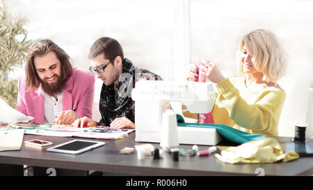 Lächelnd Geschäftsfrau maßgeschneiderte sitzen an der Nähmaschine und handgefertigte Kleidung, während Marketing Assistant arbeiten an neuen Projek Stockfoto