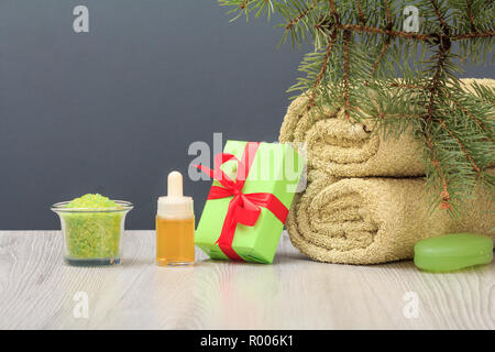 Spa Zusammensetzung mit weichen Frotteehandtuch, Flasche mit Aromaöl, Geschenkbox, Schüssel mit Meersalz, Seife und Fir Tree Branch auf grauem Hintergrund Stockfoto