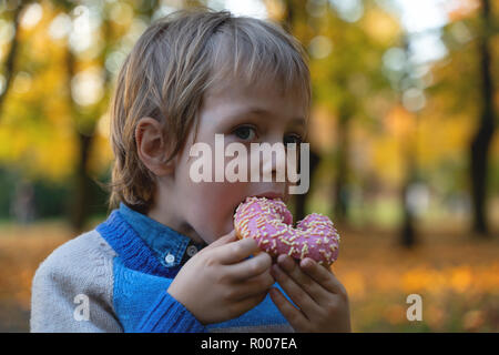Junge kaukasier Junge 5 Jahre alt Essen Donut im Freien Nahaufnahme. Kindheit. Stockfoto