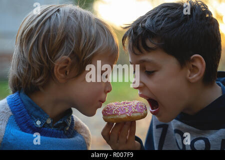 Zwei kaukasischen Jungen essen ein Donut im Freien Nahaufnahme. Kindheit. Stockfoto