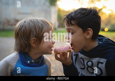 Zwei kaukasischen Jungen essen ein Donut im Freien Nahaufnahme. Kindheit. Stockfoto
