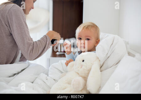 Mutter und Kind im Schlafanzug, am frühen Morgen, Mama kümmert sich um ihre kranke Kind Junge. Baby im Bett mit Fieber und laufende Nase Stockfoto