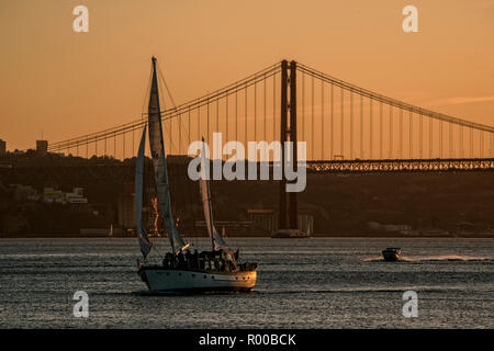 Atmosphäre am Abend auf den Fluss Tejo (Rio Tejo) mit Segelboot und die Ponte 25 de Abril Suspension Bridge, Lissabon, Portugal. Stockfoto