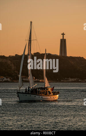 Atmosphäre am Abend auf den Fluss Tejo (Rio Tejo) mit Segelboot und Jesus Statue Cristo Rei, Lissabon, Portugal. Stockfoto