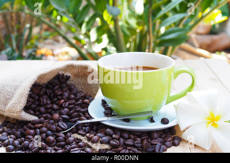 Grüner Kaffee Tasse mit sackleinen Sack mit Kaffeebohnen auf hölzernen Tisch Stockfoto