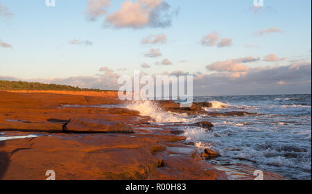 Am Morgen die Sonne scheint auf die rote Küste von Prince Edward Island, Kanada. Die roten Klippen und Strände Leuchten mit der Wärme der Sonne. Stockfoto