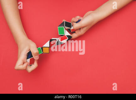 Bunte magic snake Lineal twist puzzle Formen in Kinderhand auf rotem Hintergrund. Stockfoto