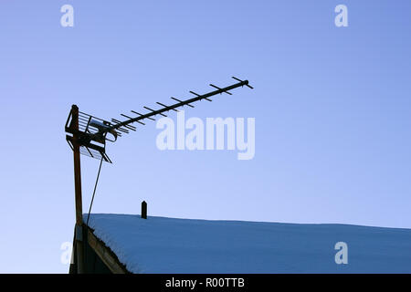 Die Fernsehantenne auf dem verschneiten Dach des alten Hauses Stockfoto