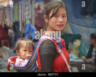 Junge vietnamesische Blume H'mong Bergvolk Schönheit trägt auf ihrem Rücken eine Nase - Kommissionierung Baby Mädchen in eine gestickte traditionelle Babytragetuch. Stockfoto