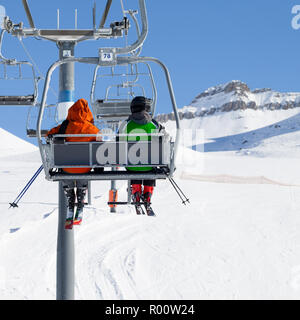 Zwei Skifahrer gehen auf der Sesselbahn und verschneite Skipiste an sonnigen Wintertag. Kaukasus, Georgien, Region Gudauri. Stockfoto