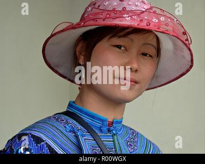 Junge vietnamesische H'Mong ethnische Minderheit Bergvolk Frau mit rosa Sonnenhut und bestickte traditionelle H'Mong Kleidung in Blau sieht in die Kamera. Stockfoto