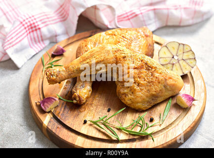 Köstliche Brathähnchen Bein oder Chicken Drumsticks auf einer hölzernen Schneidebrett. Hohe Betrachtungswinkel und frischem Rosmarin und Knoblauch. Nahaufnahme, Ansicht von oben. Stockfoto