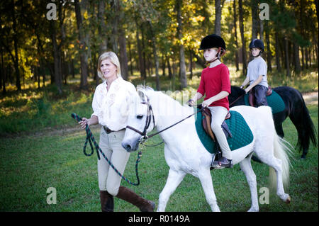 Mitte der erwachsenen Frau gehen mit ihrer Tochter und ihrem Sohn, wie sie Ponys reiten. Stockfoto