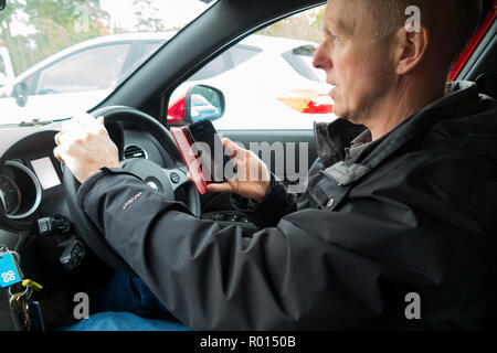 Im mittleren Alter Fahrer während der Fahrt telefonieren und mit einem mobilen Telefon Telefon/Hand Hörer der Aufruf, der eine illegale Handlung zu wählen und zu Punkten auf Lizenz führen. Großbritannien (103) Stockfoto