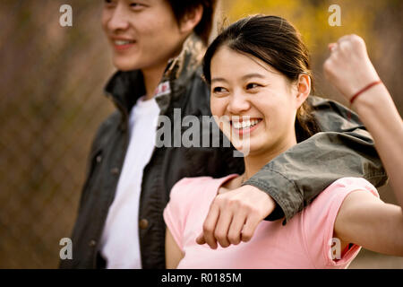 Junge erwachsene Frau ihre Muskeln zeigen, während sie von ihrem Freund umarmte. Stockfoto