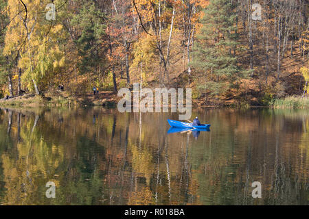 Schönen herbstlichen Wald spiegelt sich in den ruhigen Wassern des Sees, mit einem Fischer in einem blauen Boot Stockfoto