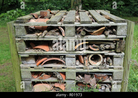 Bug Hotel in einem Rahmen von Holzpaletten mit Baumstämmen, Ästen, Bambusstämmen und gebrochenen Ton Blumentöpfe umgeben von Gras mit Bäumen. Stockfoto