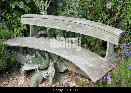 Traditionelle Holz- gebogene Park Sitz in einer schattigen Ecke von Pflanzen umgeben. Stockfoto