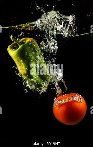 Gemüse, Tomaten und Paprika in Wasser spritzen auf schwarzem Hintergrund Stockfoto