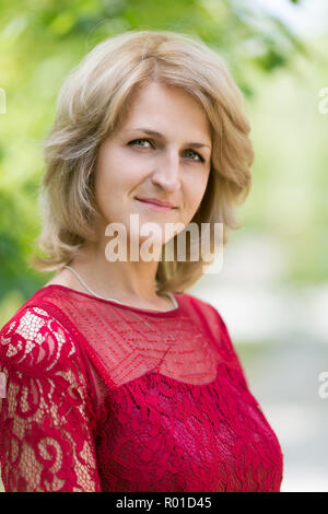 Europäische Frau 40 Jahre alt in einem roten Kleid auf der Natur. Stockfoto