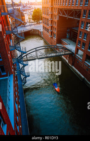 Kleines Boot unter der Brücke über den Kanal zwischen roten Backsteinbauten in der Speicherstadt Die Speicherstadt in Hamburg in der Goldenen Stunde Sonnenuntergang Licht, Deutschland. Ansicht von oben Stockfoto