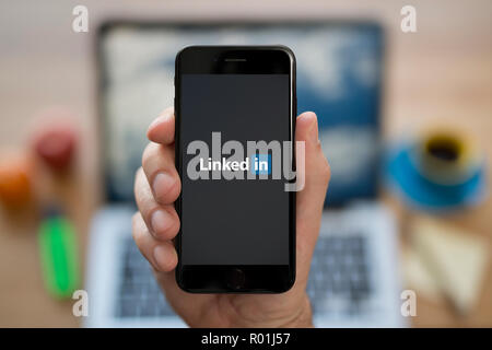 Ein Mann schaut auf seinem iPhone die zeigt die LinkedIn logo, während saß an seinem Computer Schreibtisch (nur redaktionelle Nutzung). Stockfoto