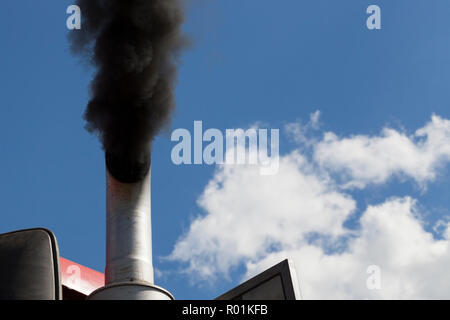 Schwarzer Rauch gegen den blauen Himmel kommen aus dem Auspuffrohr des Traktors während des Betriebs des Motors Stockfoto