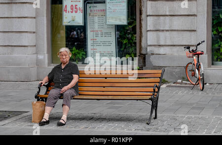 WUHAN, China - September 08, 2018: Alte asiatische Frau sitzt auf den alten Stuhl in den Park. Sie sehen aus wie warten auf jemanden. Stockfoto