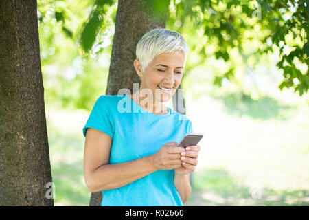 Portrait von sportlichen ältere Frau mit Handy im Park an einem sonnigen Tag Stockfoto