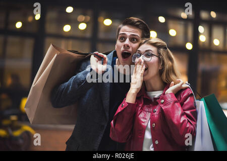 Schönes Paar mit Einkaufstüten spricht und lächelnd, während sie Shopping in der Mall konzentrieren sie sich auf die überraschten Frau.