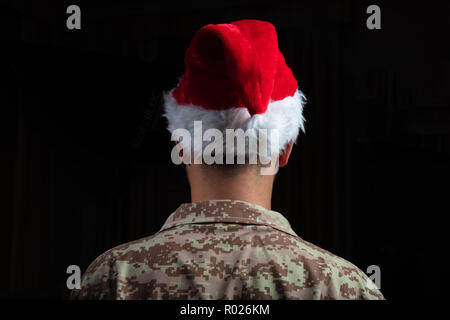 Weihnachten und Armee. Junge Soldat trägt santa hut stehend auf schwarzem Hintergrund Stockfoto