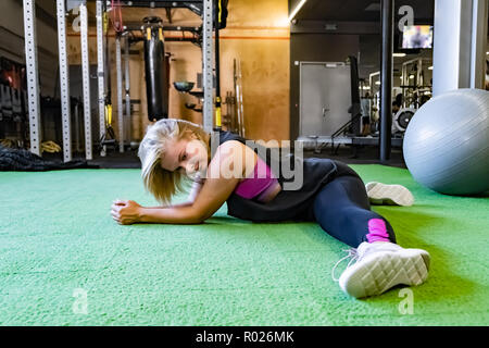 Junge passende Frau an der Turnhalle tun Split trainieren. Sportlerin im Fitnessraum trainieren Sie auf Seite 2 Stockfoto