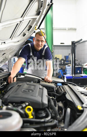 Kfz-Mechaniker prüft den Motor eines Fahrzeugs - im Hintergrund Auto auf die Hebebühne - Arbeitsplatz und Beruf Stockfoto