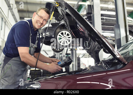 Lächelnd Automechaniker in einer Werkstatt - Motor Reparatur und Diagnose an einem Fahrzeug Stockfoto