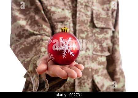 Weihnachten und Armee. Junge Soldat hält ein rotes christmas Ball stehend auf weißem Hintergrund Stockfoto