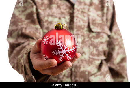 Weihnachten und Armee. Junge Soldat hält ein rotes christmas Ball stehend auf weißem Hintergrund Stockfoto