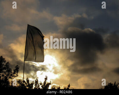 Große rectangler Flagge an einem Summer Music Festival. Bäume im Vordergrund und die Sonne durch die Wolken im Hintergrund Stockfoto