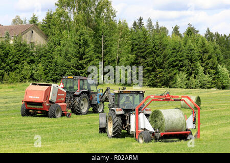 Uurainen Finnland - Juni 15, 2018: Umhüllung Heuballen mit Lamborghini Traktor und Vicon BV 1700 Wrapper, Traktor und Lely Welger Rundballenpresse auf Hintergrund. Stockfoto