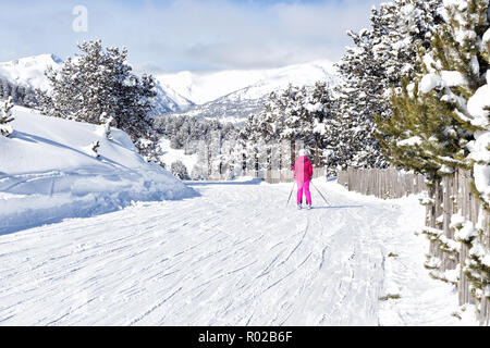 Das Mädchen ist Skifahren auf der malerischen flachen Hang in den Bergen unter den Tannen. Leuchtend rosa Anzug auf das Mädchen, das eine Menge flauschige Schnee und die Spitzen von Stockfoto