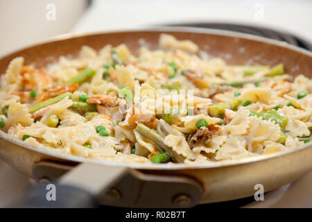 Lecker aussehenden Nudelgericht in einer Pfanne gekocht und gerührt, mit Lachs, Pasta, Spargel und Erbsen Stockfoto