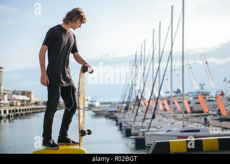 Curly Mann stand am Pier mit Longboard und suchen bei Yacht Stockfoto