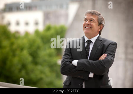 Geschäftsmann mit verschränkten Armen blickt auf und lächelt, als Er posiert für ein Portrait einer Stadt, Balkon. Stockfoto